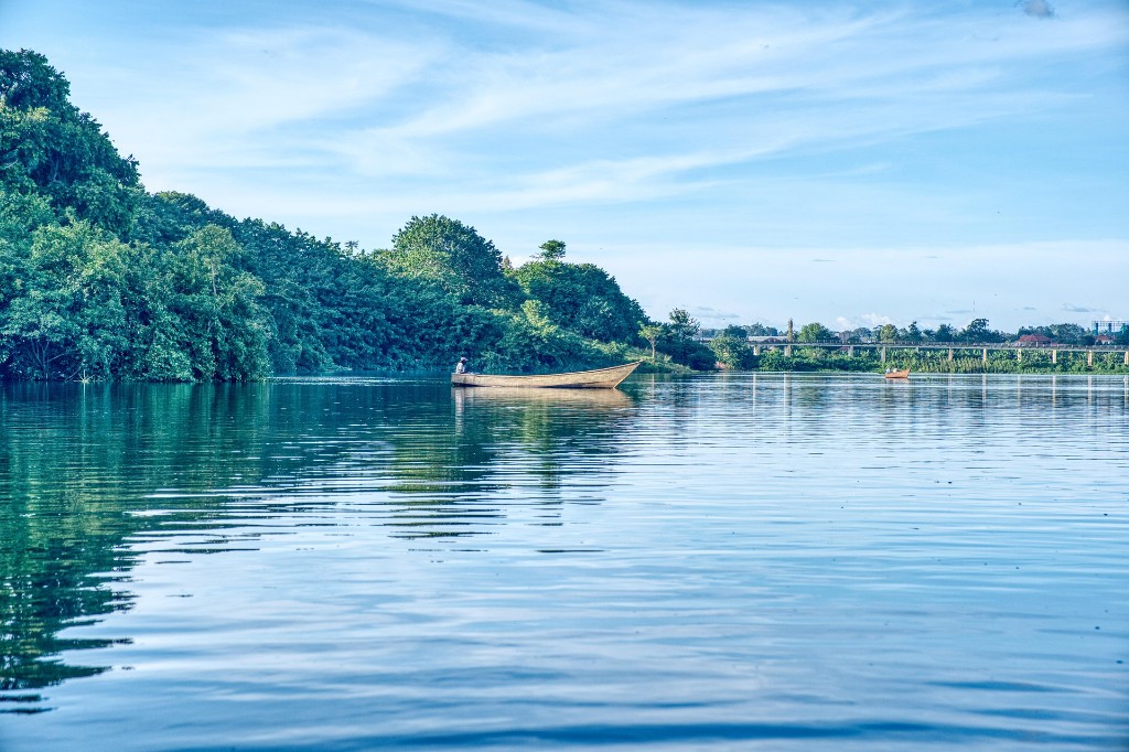 A person in a traditional wooden boat on a calm river with lush green banks in Uganda
